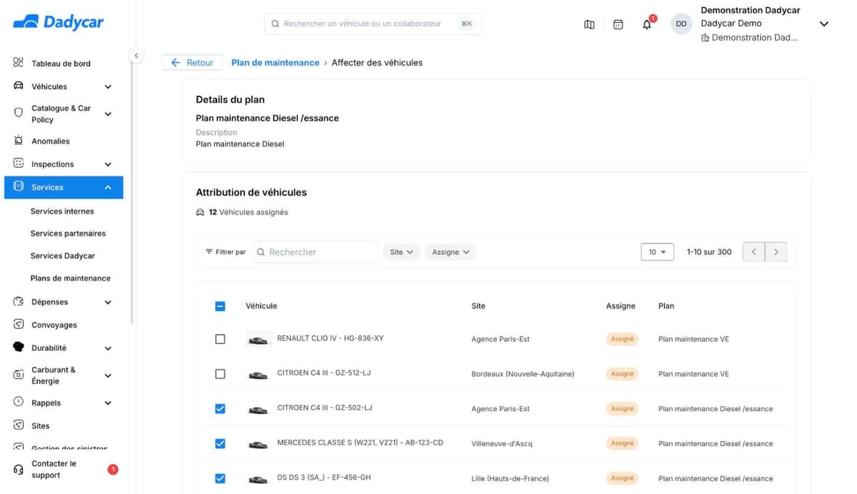 La page Affecter des véhicules : le plan « Plan maintenance Diesel / essence » dans le bloc Details du plan, puis le bloc Attribution de véhicules avec « 12 Véhicules assignés », une recherche, les filtres Site et Assigné, et une liste de véhicules à cocher avec leur site, un repère « Assigné » et le plan auquel chacun est déjà rattaché.